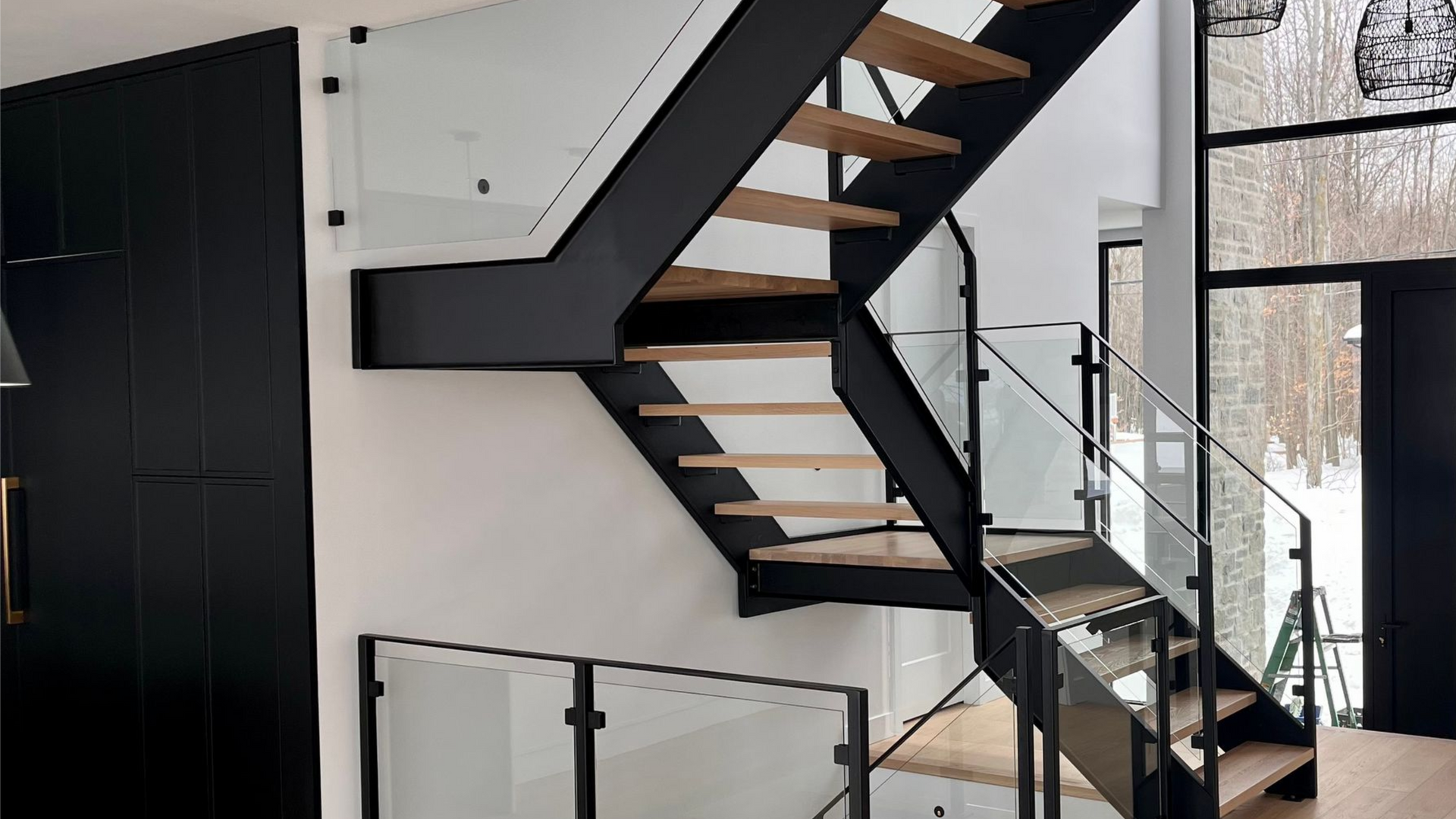 Escalier moderne avec structure en métal noir, rampes en verre et marches en bois.
