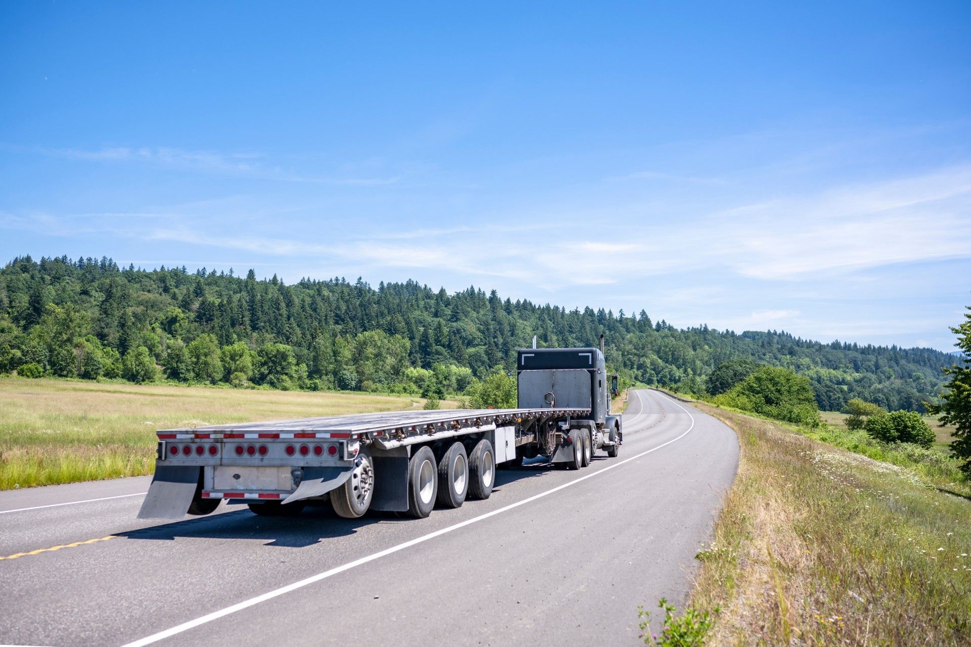 A semi truck is driving down a highway next to a field.