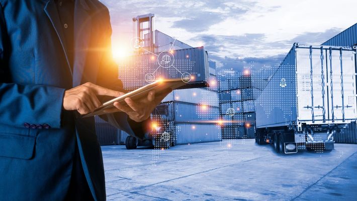 A man in a suit is holding a tablet in front of a warehouse.