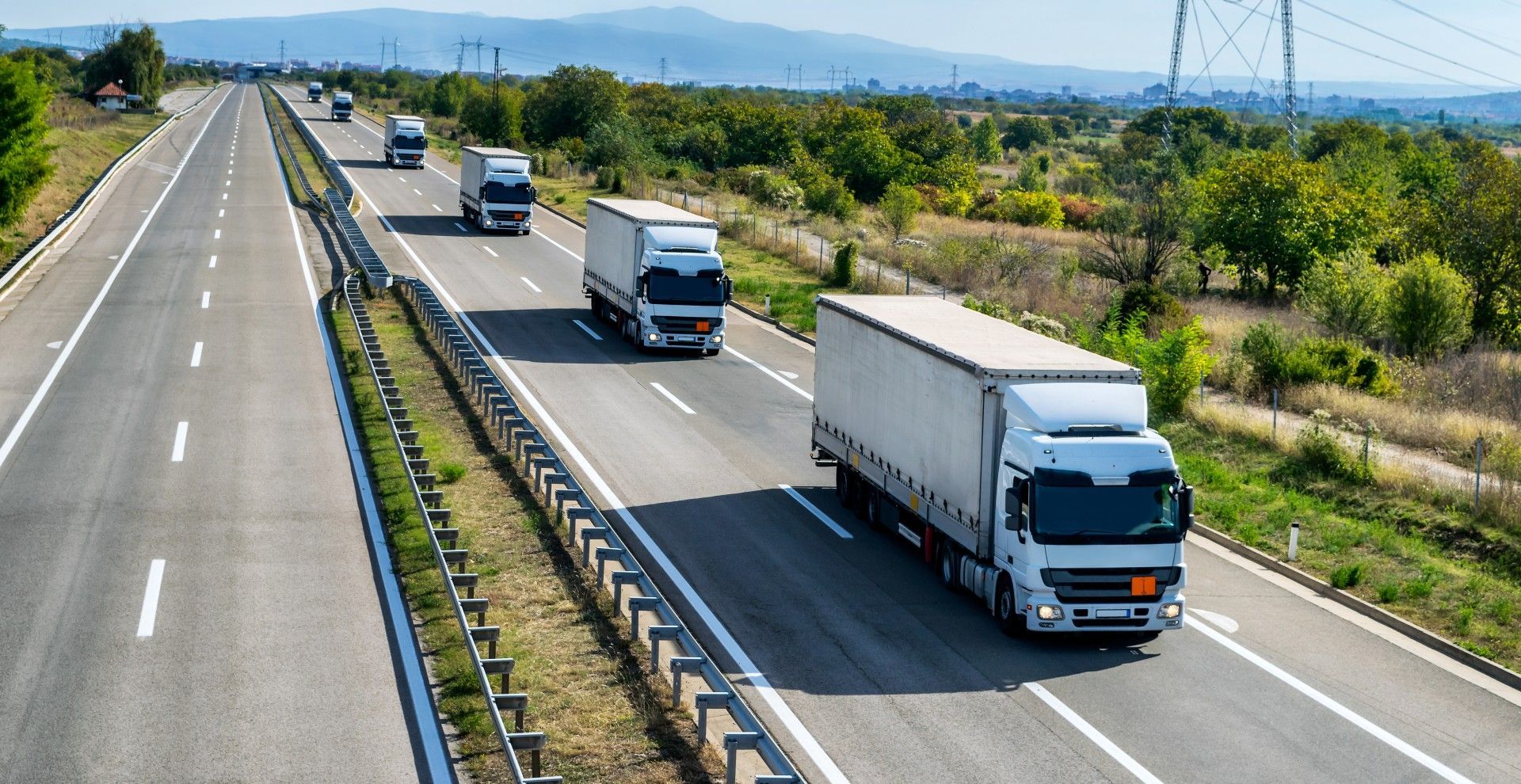 A row of semi trucks are driving down a highway.