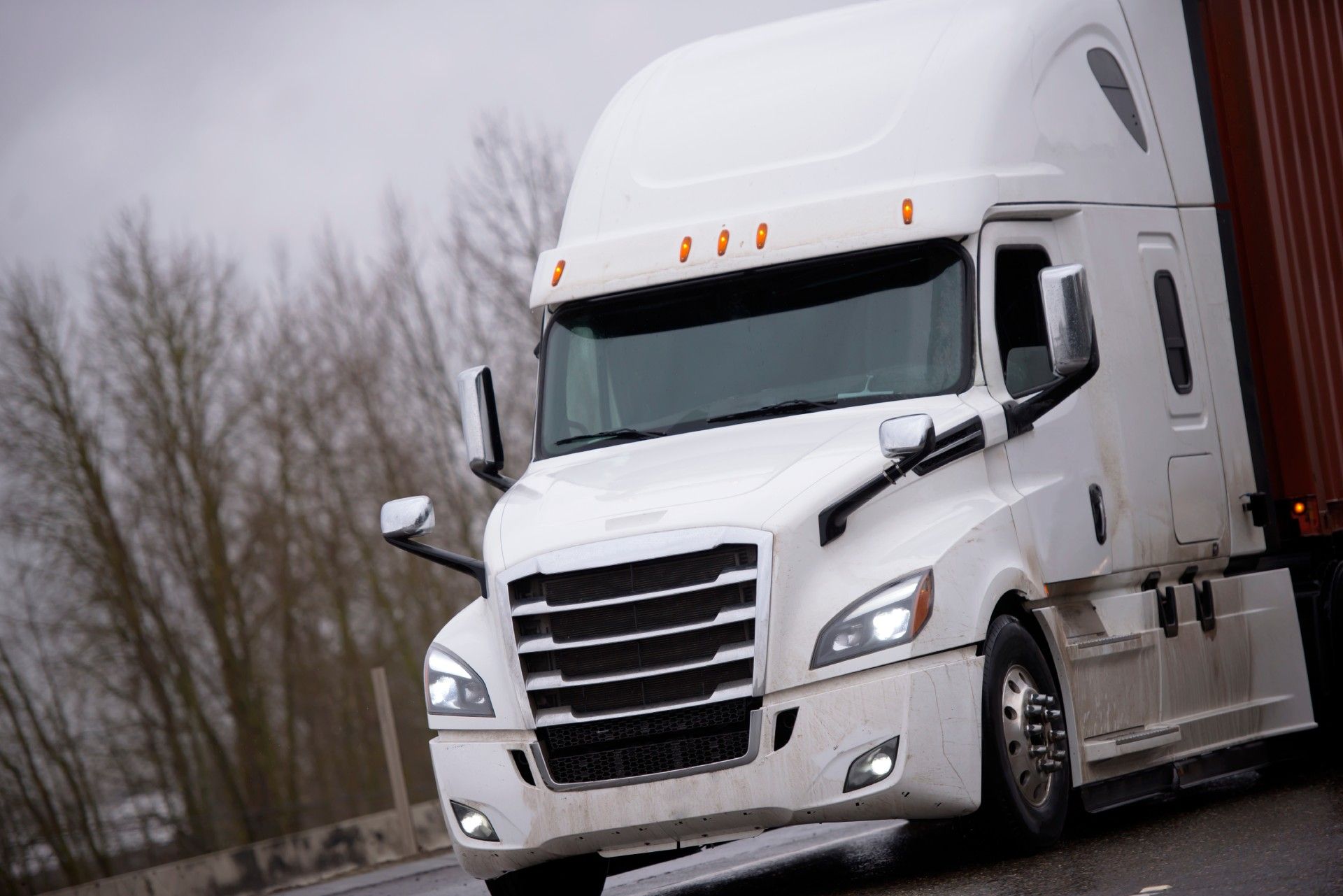 A white semi truck with a red trailer is driving down a road.