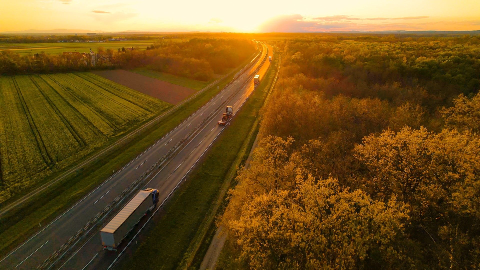 An aerial view of a highway with trucks driving down it at sunset.