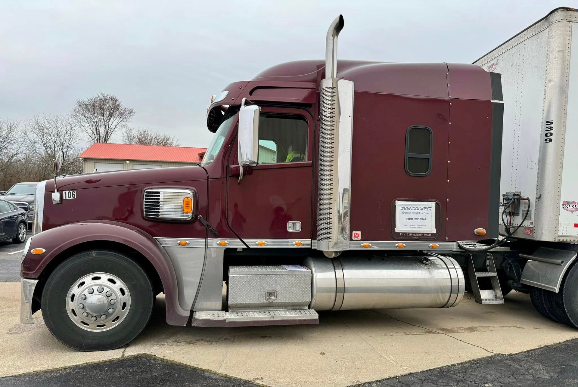 A red semi truck is parked next to a white trailer.