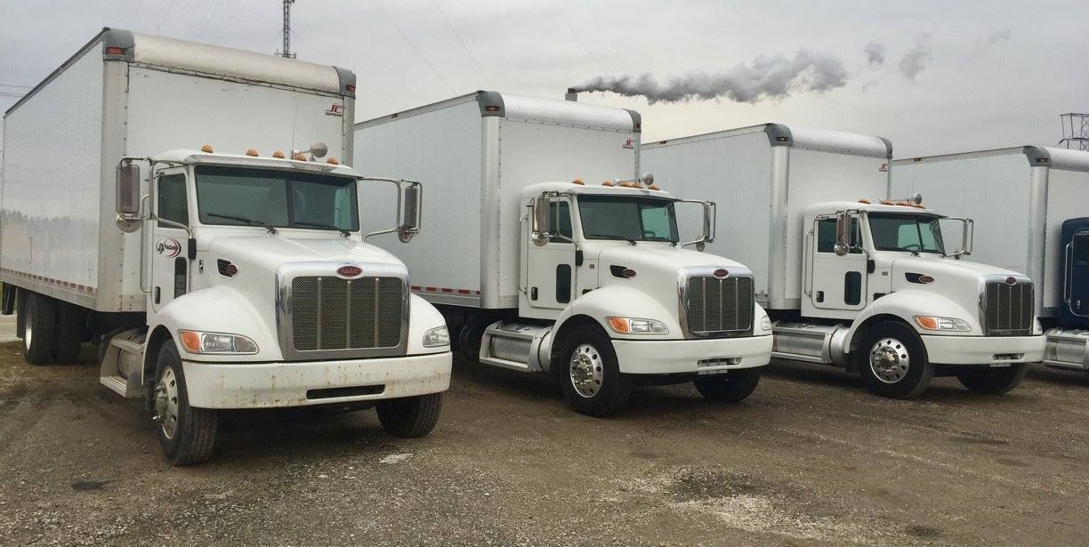 Three white semi trucks are parked next to each other in a gravel lot.