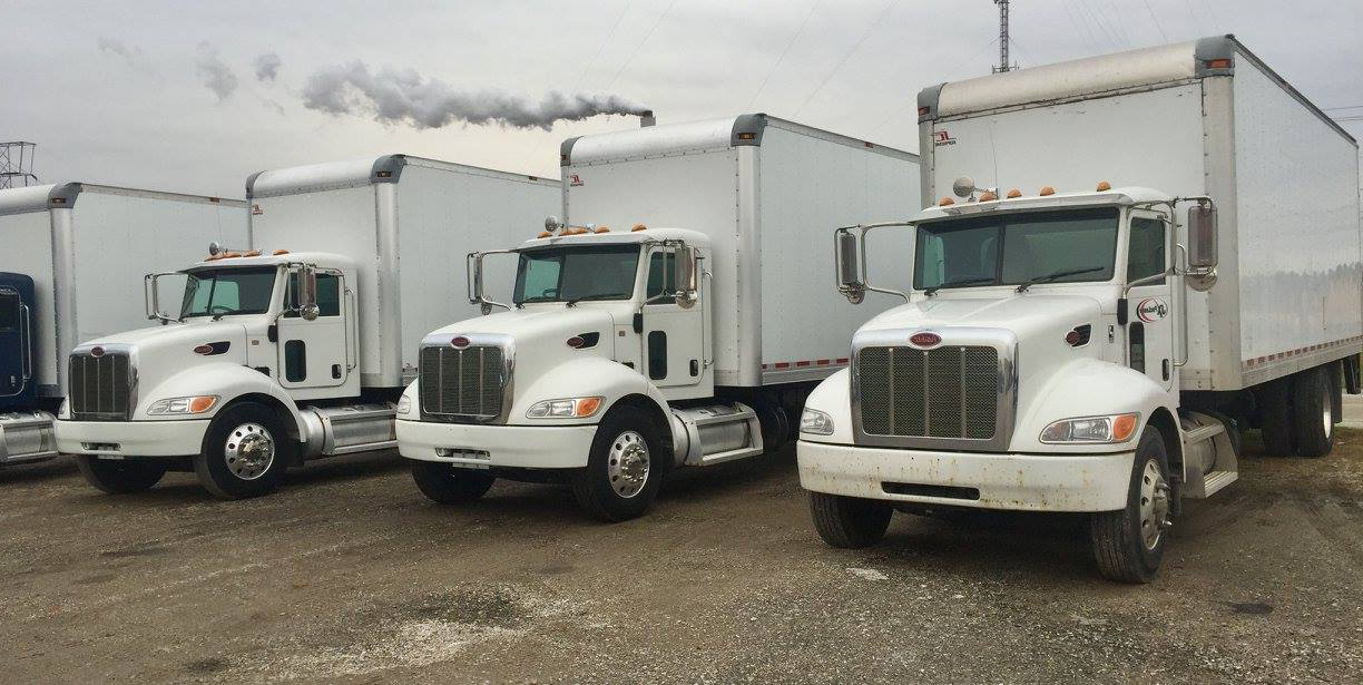 Three white semi trucks are parked next to each other in a gravel lot.