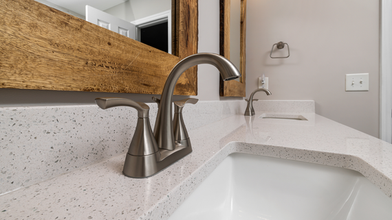Bathroom sink with brushed nickel faucet, white quartz countertop, and rustic wood-framed mirror.