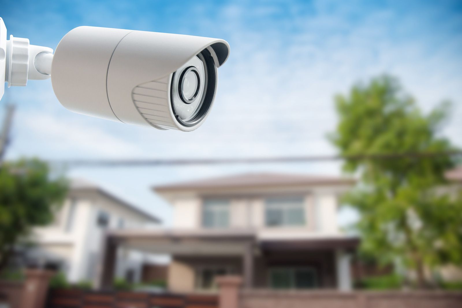 A person is holding a security camera next to a picture of a house.