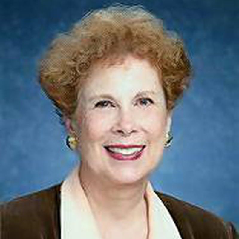 Smiling woman with short curly hair in a brown jacket against a blue studio background