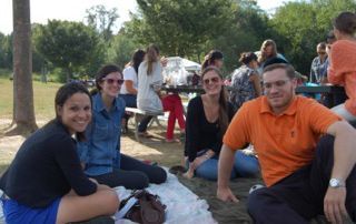 People sitting on a blanket at an outdoor picnic in a park, smiling and relaxing.