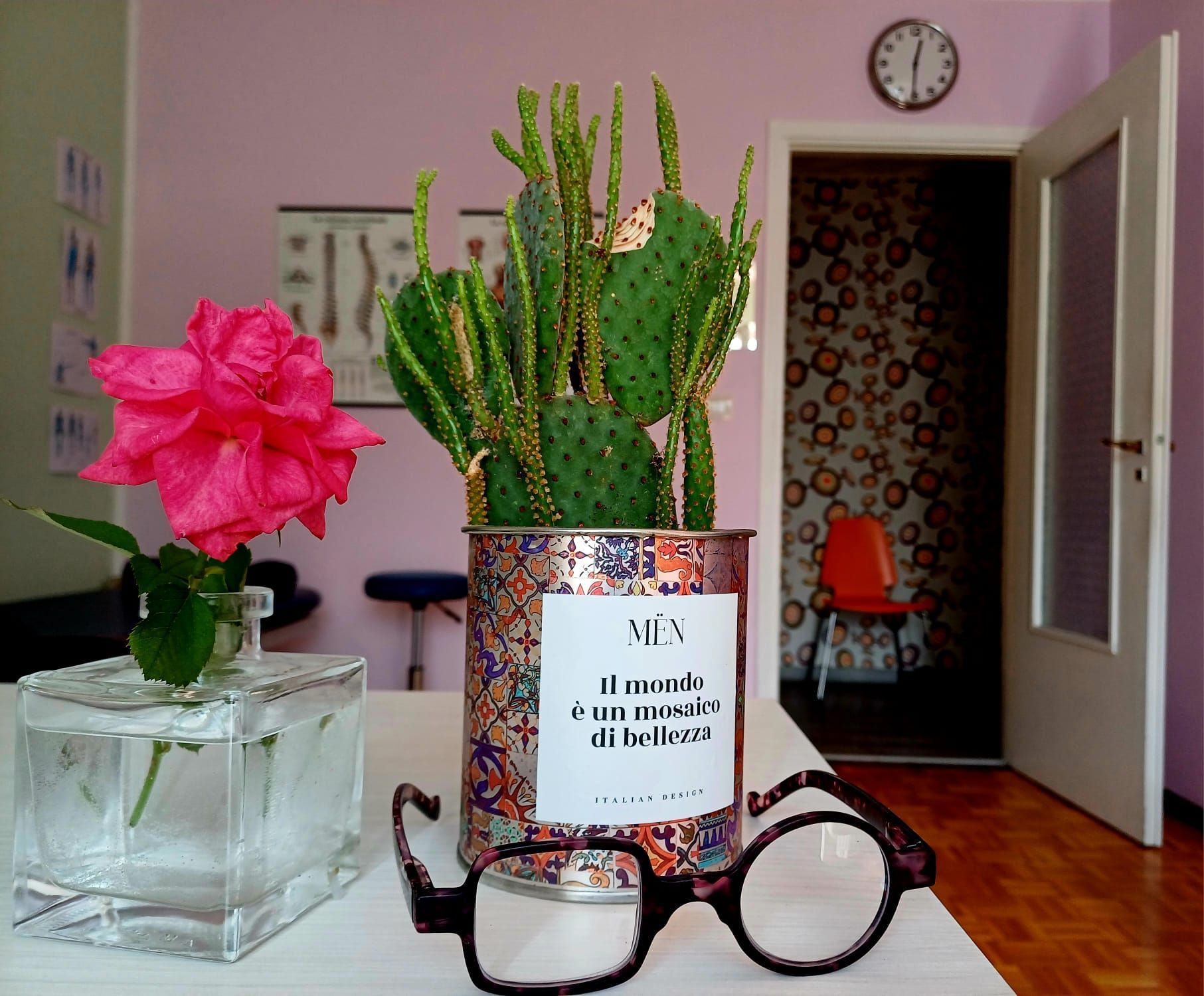 Una composizione di natura morta presenta una rosa rosa, un cactus, degli occhiali e un orologio.