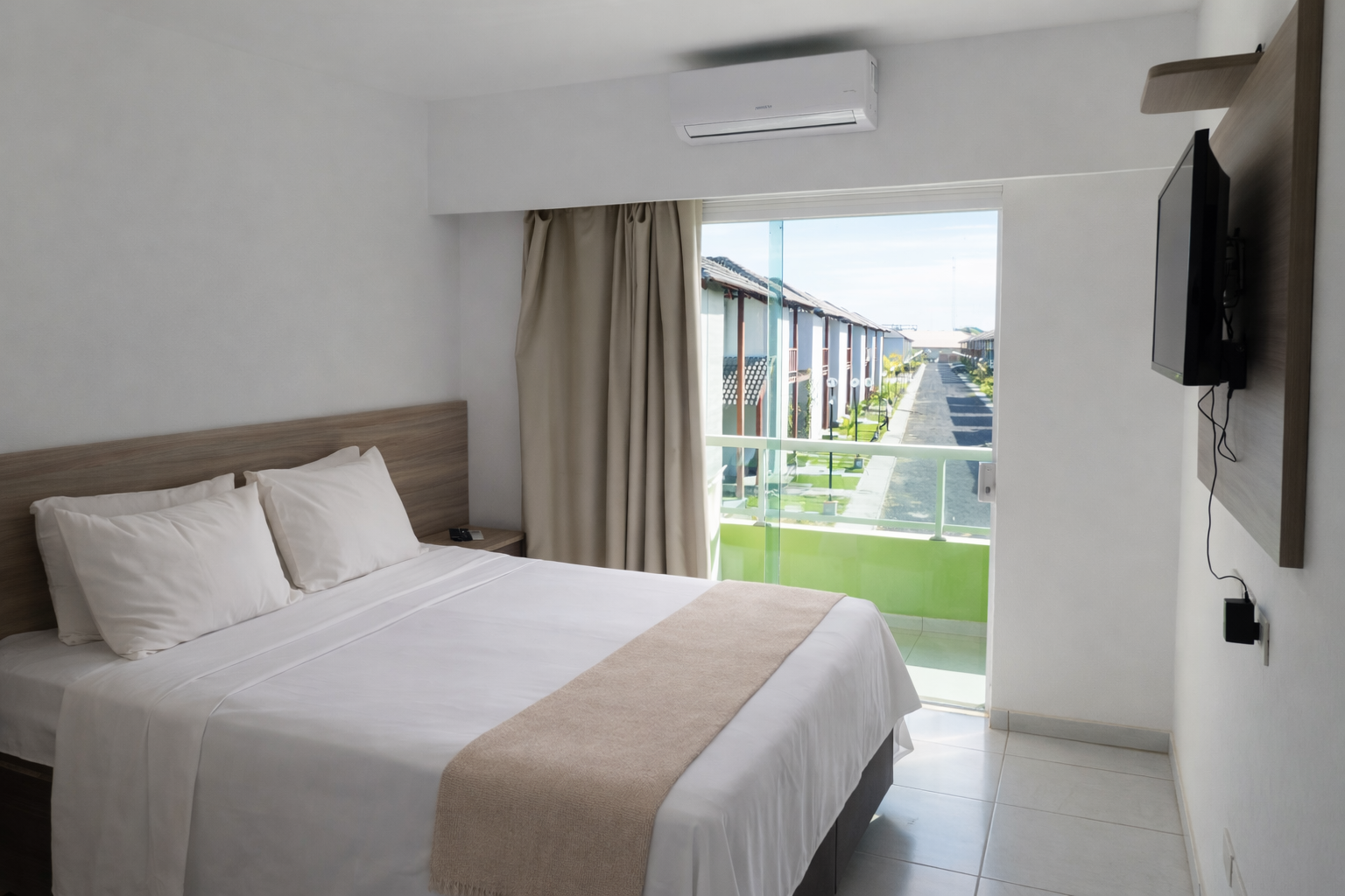 Quarto com cama, TV e janela grande com vista para um prédio.