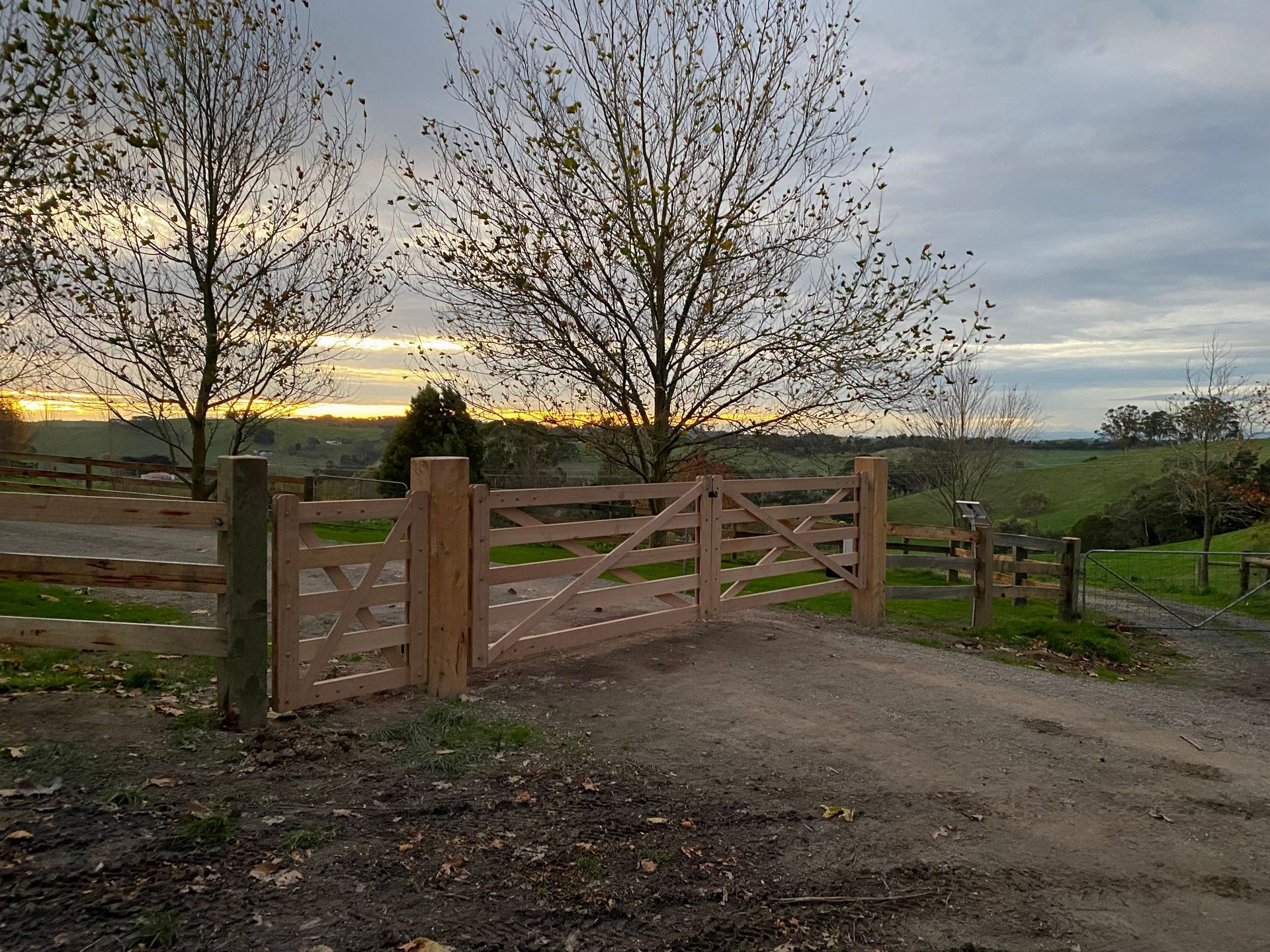A wooden gate is sitting on the side of a dirt road.
