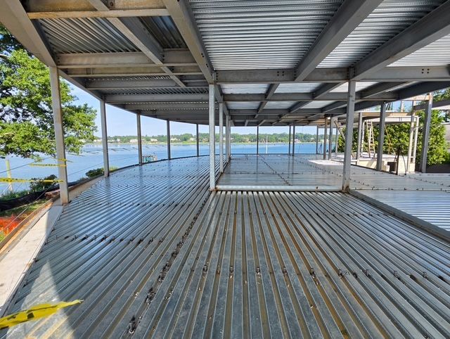 Covered waterfront deck with metal roof, slatted floor, and open views of a lake and trees