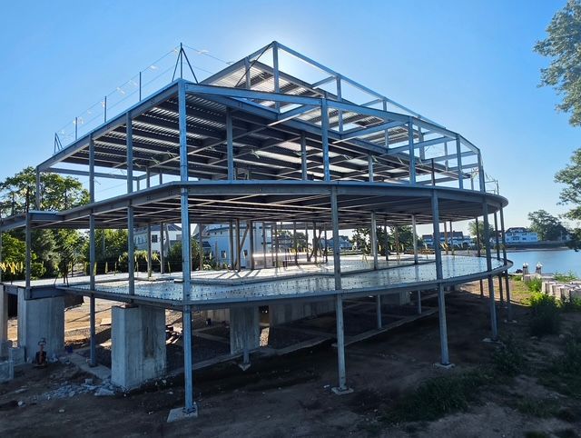 Partially built steel-frame building by the water under a clear blue sky