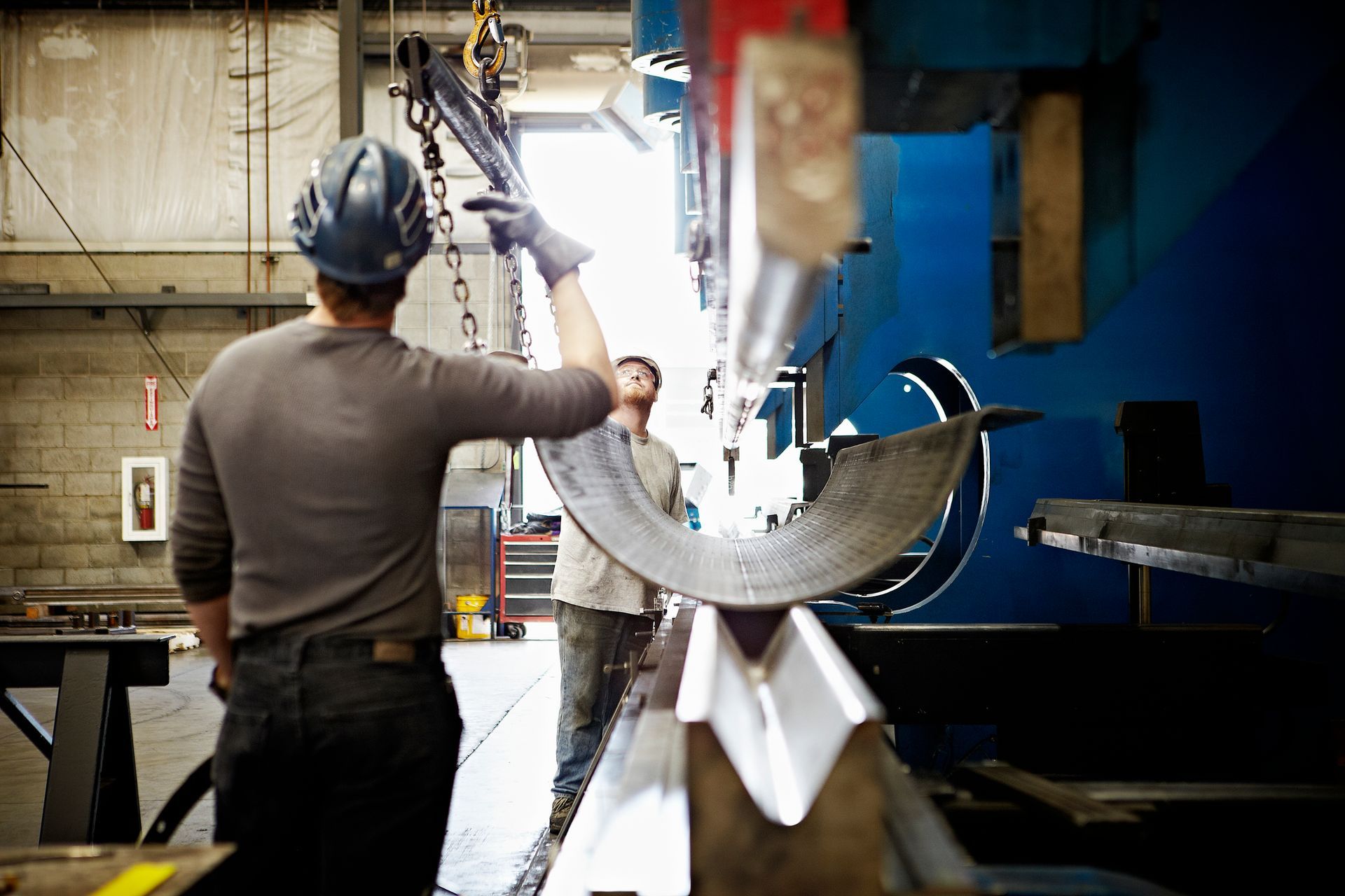 Two male professional workers adjusting position of steel in large brake press.