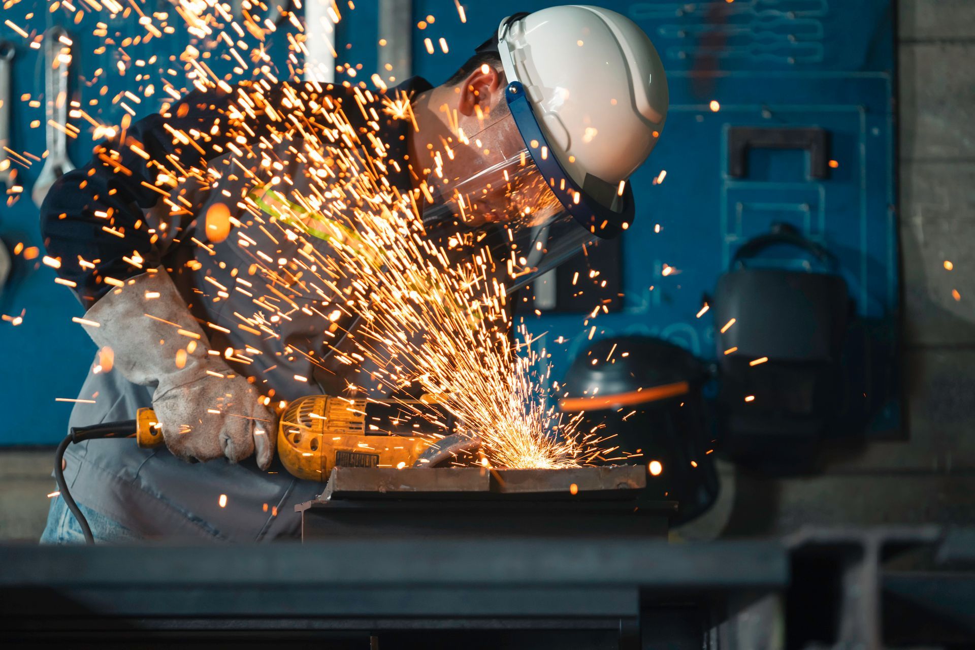 A worker in a safety helmet and gloves is using an angle grinder on a steel plate. A worker in a safety helmet and gloves is using an angle grinder on a steel plate.