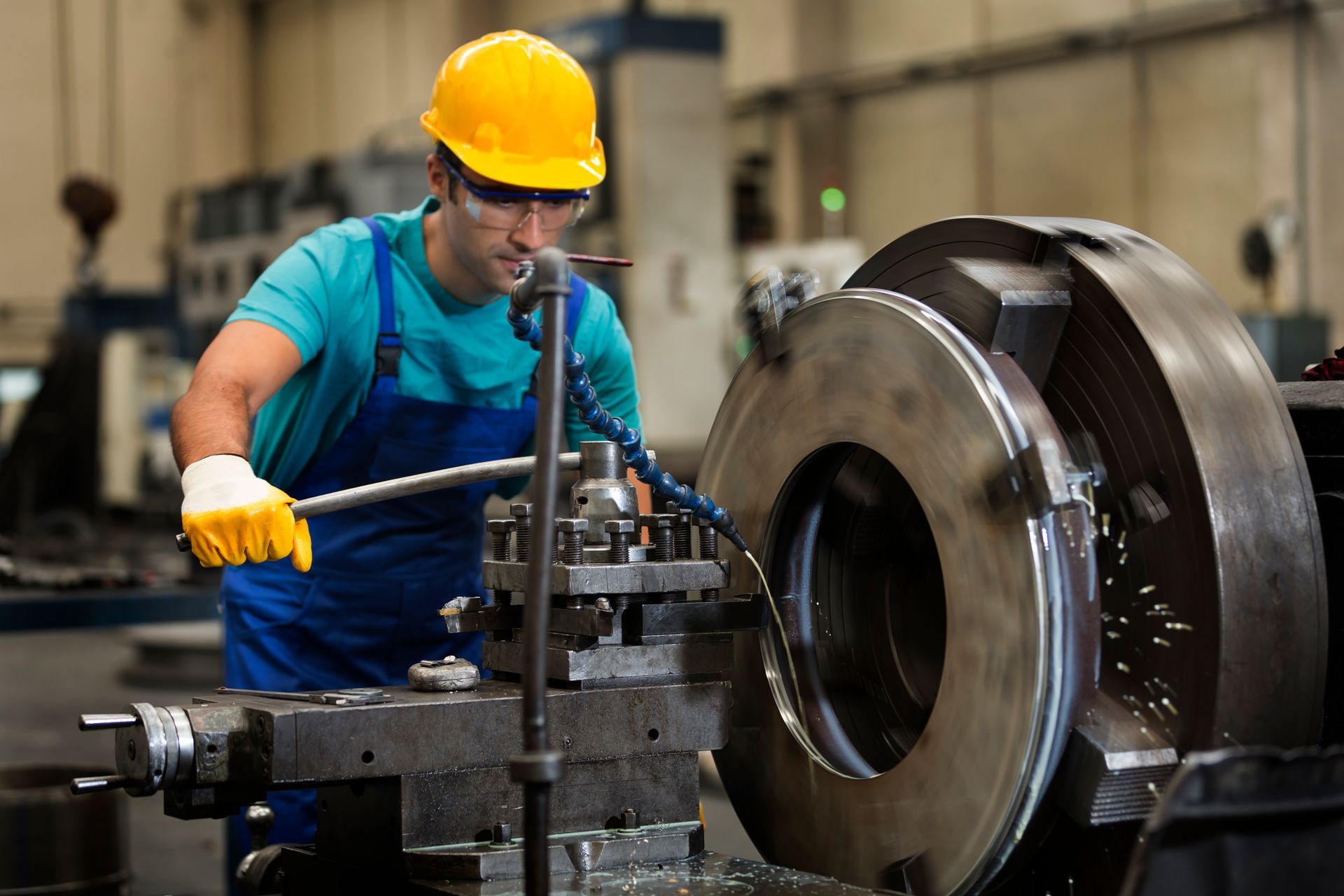 A male professional steel fabricator with yellow protective hat and gloves at a factory.