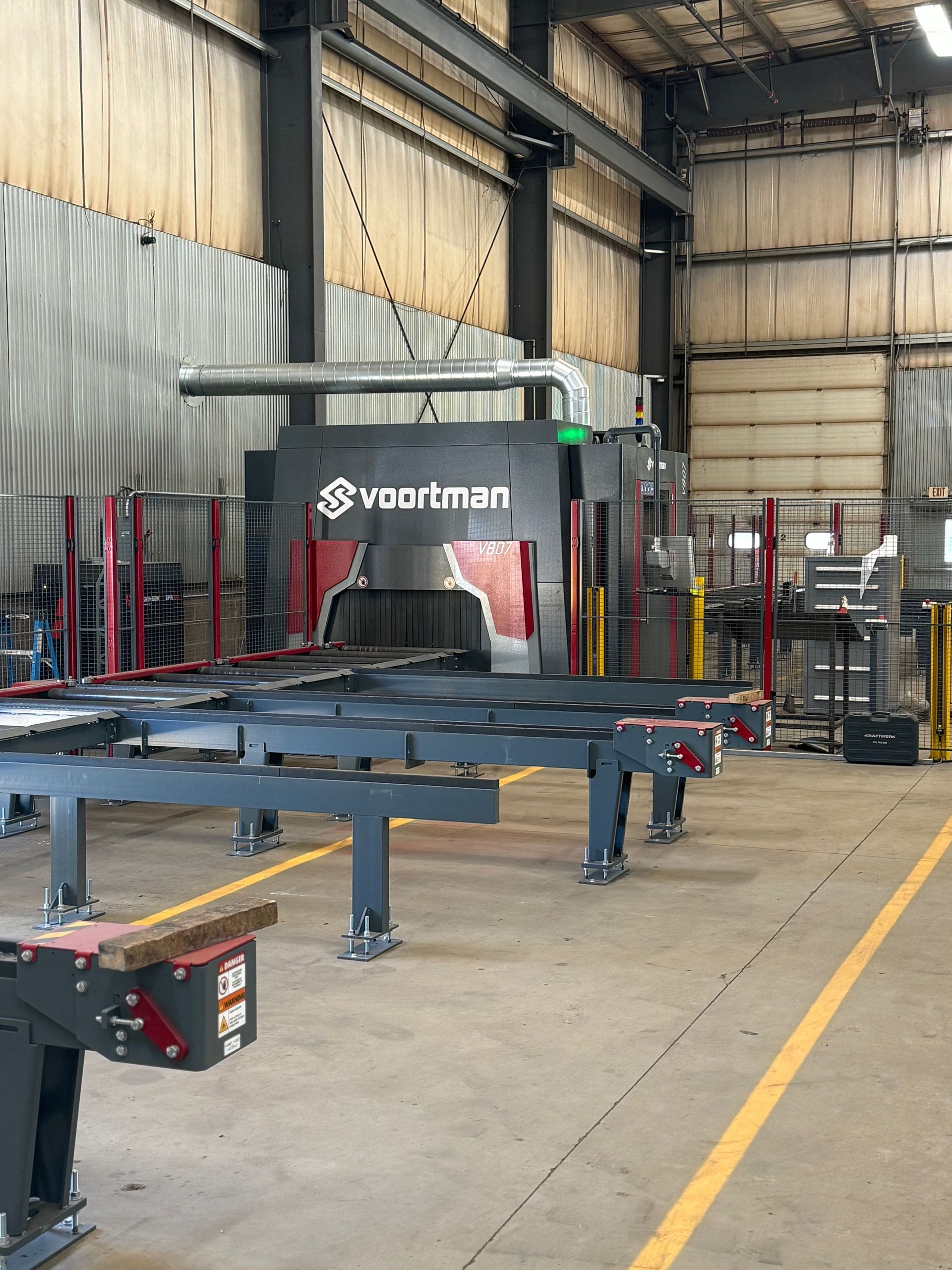A large industrial metal cutting machine with a Vaartman logo in a warehouse.