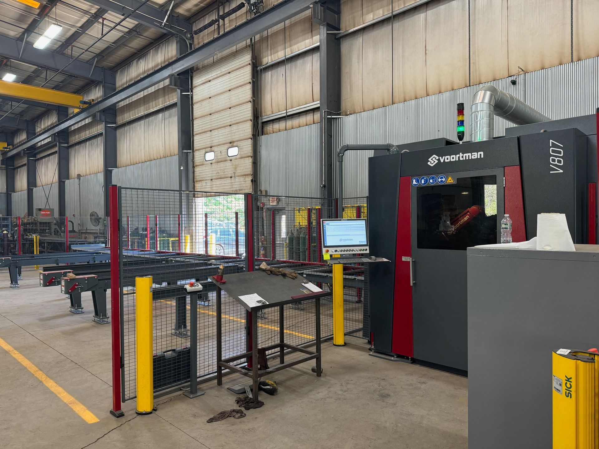 Industrial facility with a red and black CNC machine, yellow safety barriers, and a control panel.