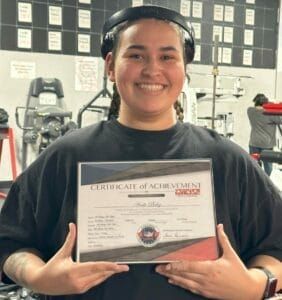 A woman is holding a certificate of achievement in a gym.