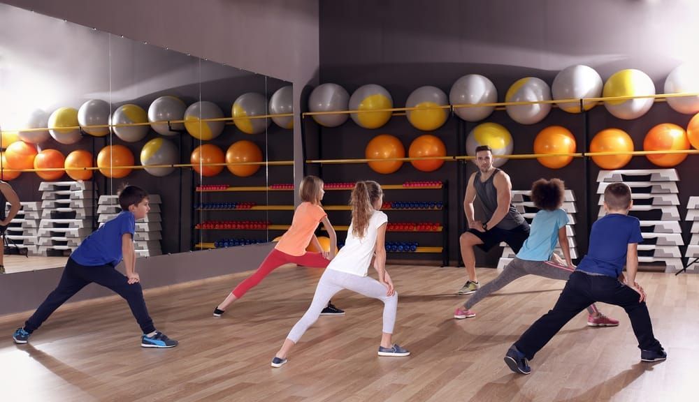 A group of children are doing stretching exercises in a gym.