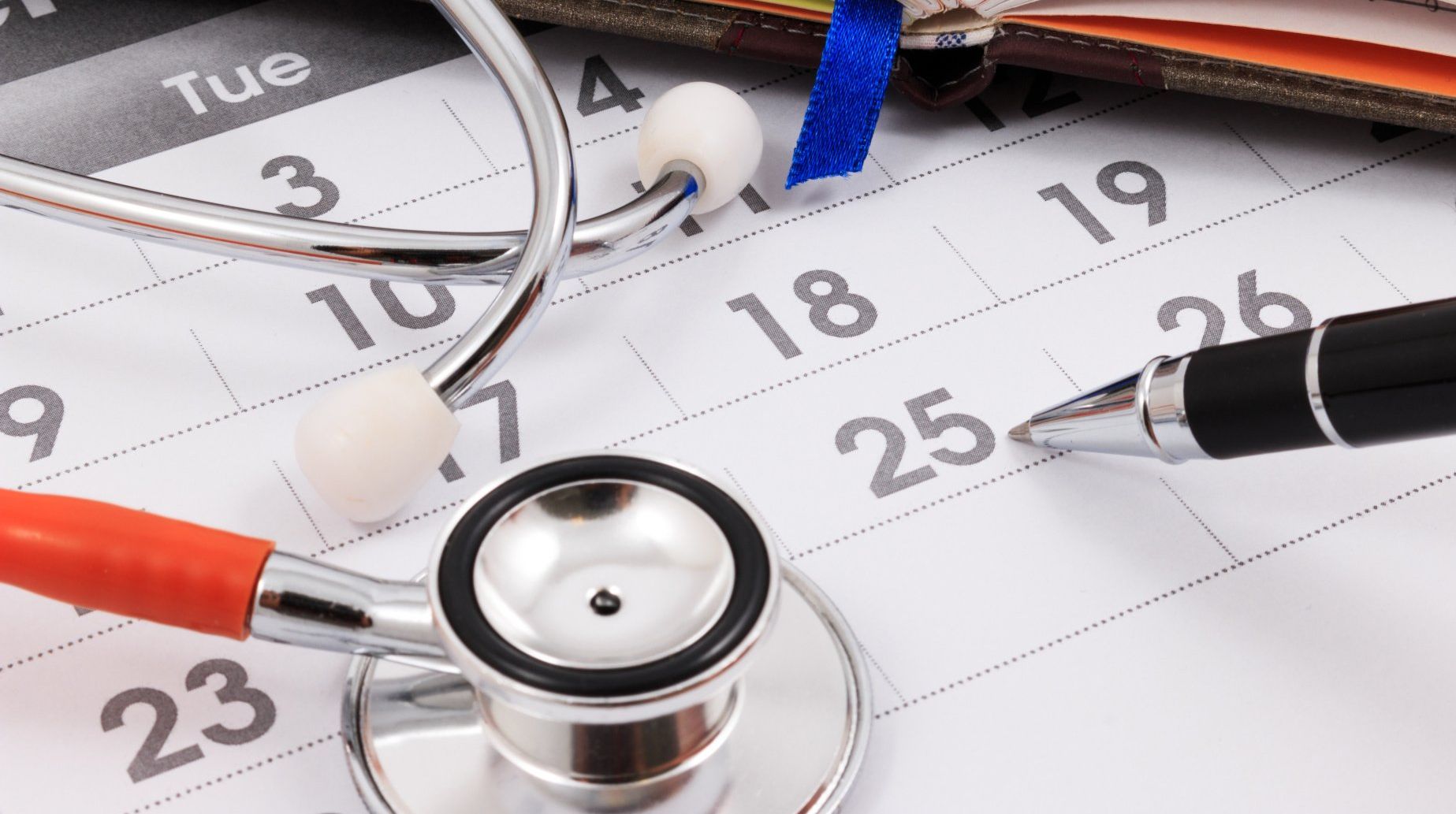 Stethoscope on a calendar, pen pointing to the 25th, suggesting a medical appointment.