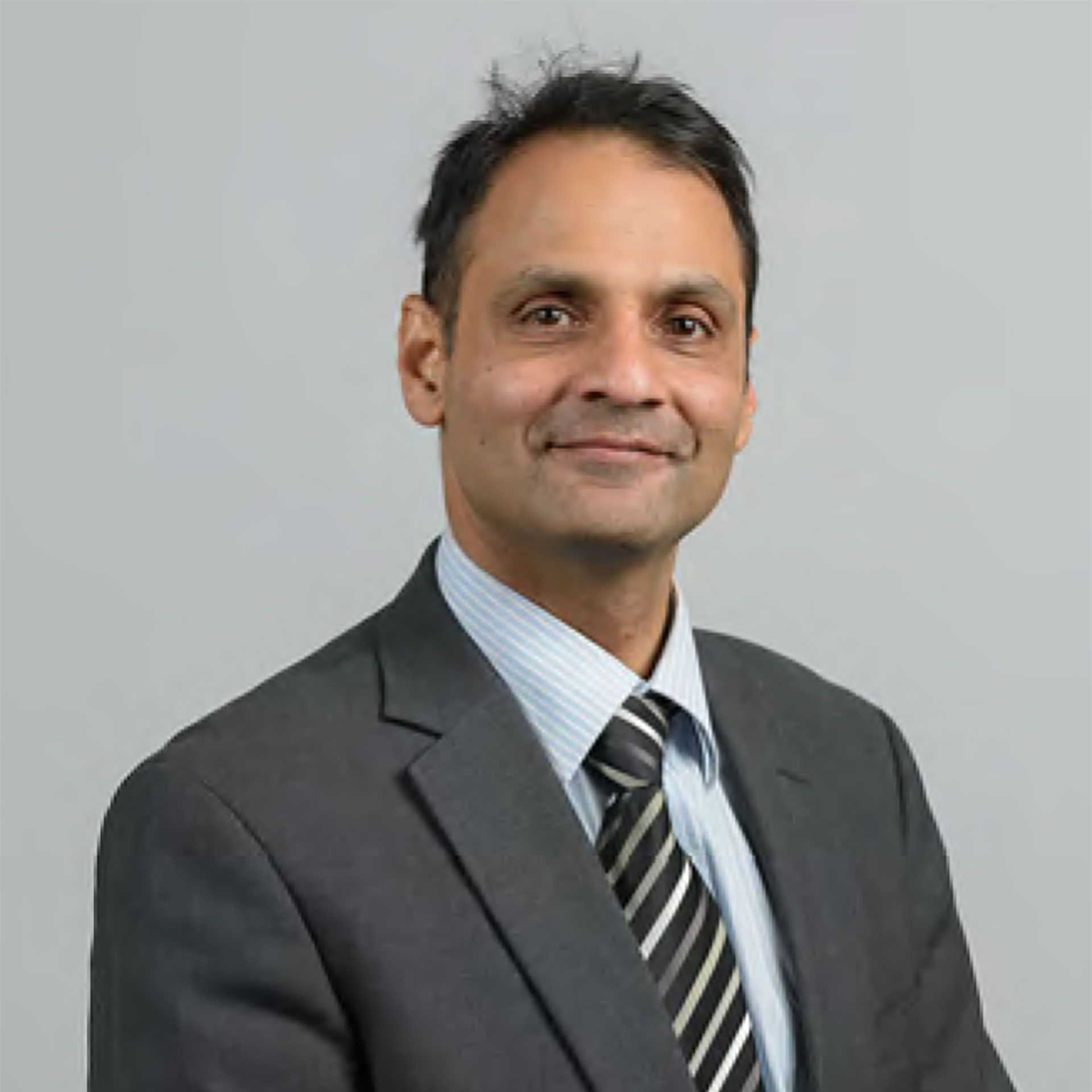 Man in suit and tie smiling, headshot against a gray background.