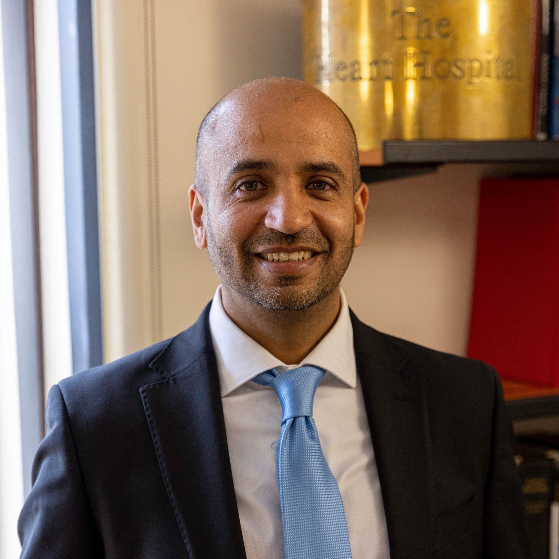 Man in suit smiling, indoors; the Heart Hospital plaque in background.