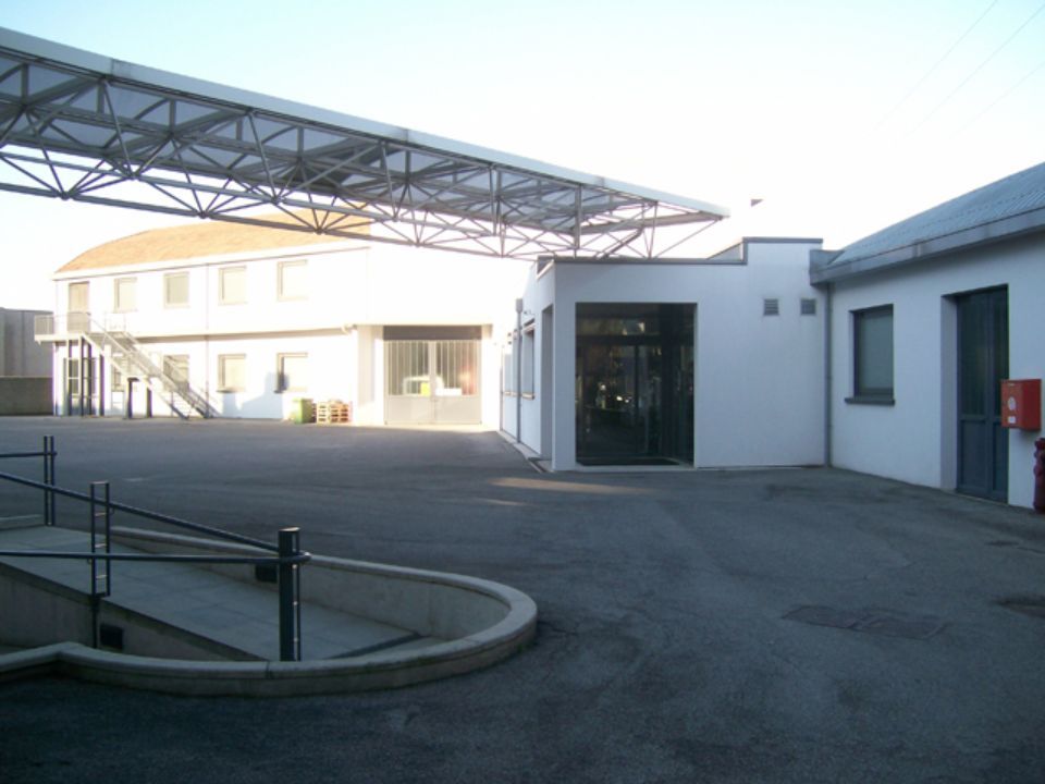 Vista esterna di un edificio bianco con passaggio coperto e parcheggio pavimentato.
