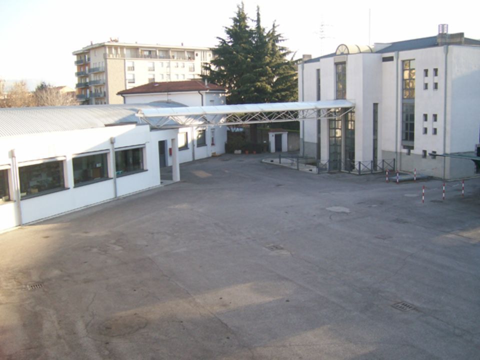 Vista esterna di un moderno edificio industriale e di un terreno pavimentato vuoto, in una giornata di sole.