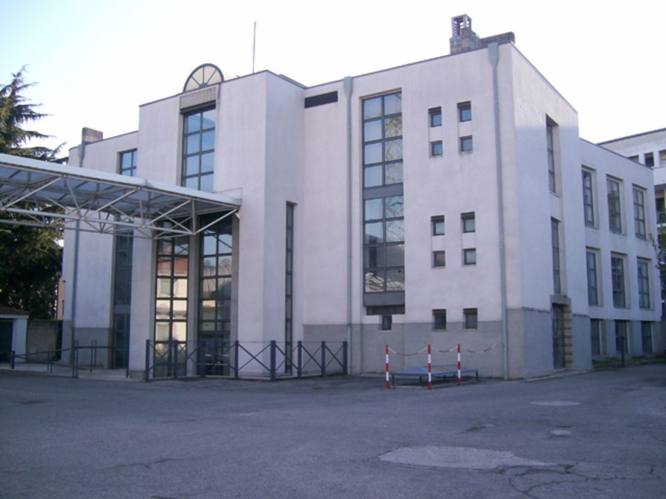Edificio bianco con finestre in vetro e passaggio coperto, in una giornata di sole.