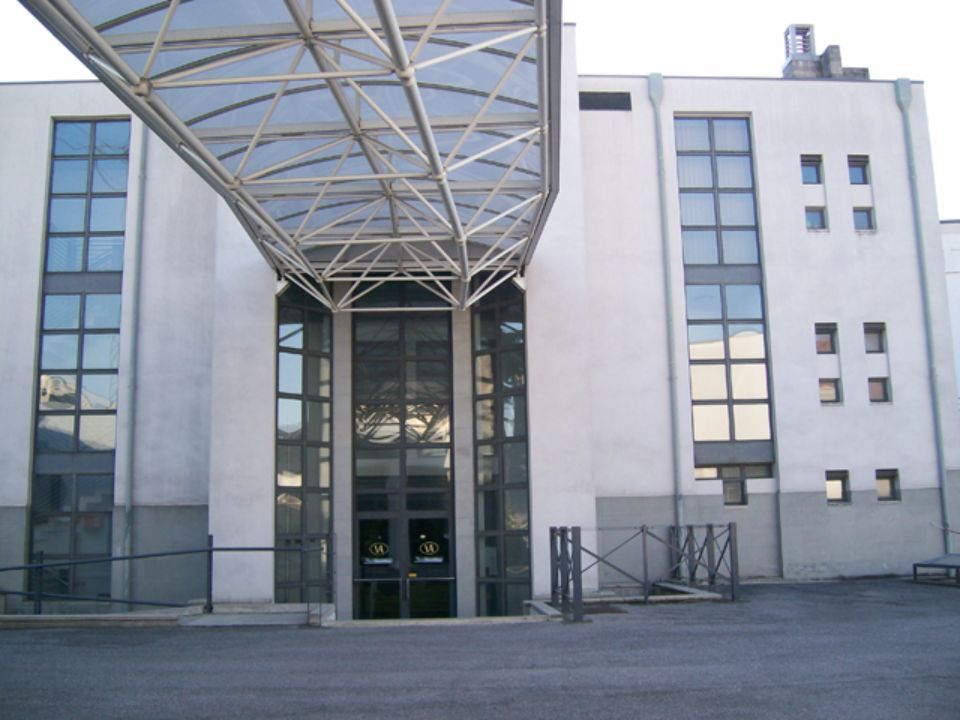 Edificio grigio con passaggio coperto che conduce a un ingresso in vetro.