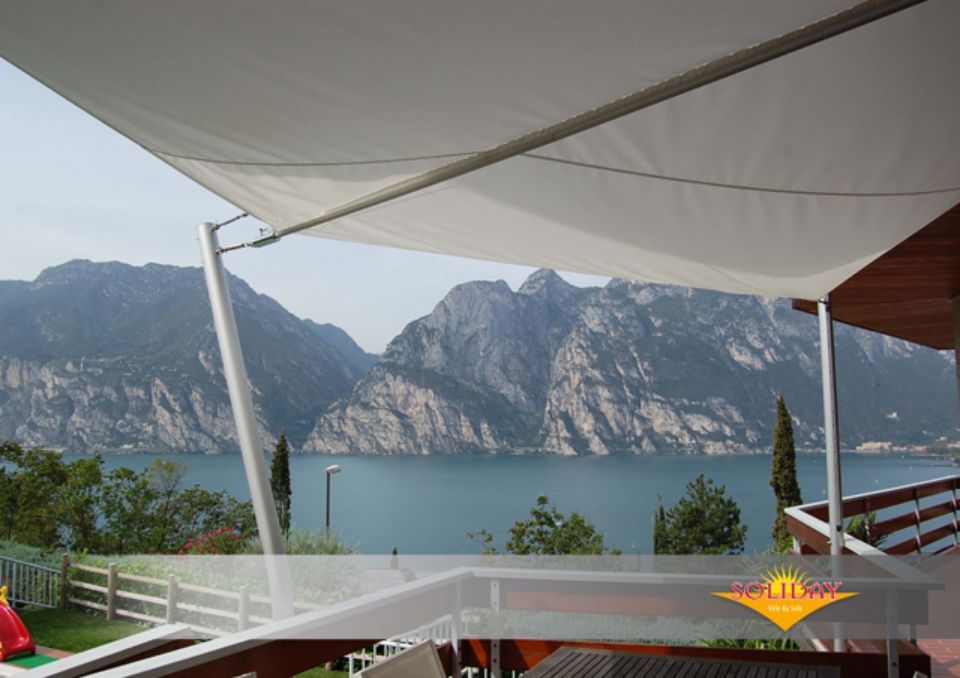 Una tettoia bianca ombreggia un patio con vista sul lago e sulle montagne.