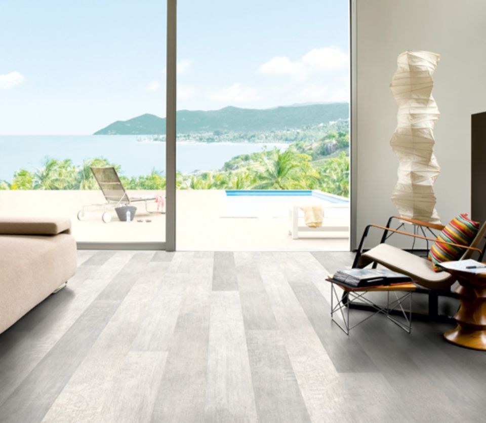 Luminoso soggiorno moderno con pavimento in legno grigio, ampia finestra con vista sulla piscina e sull'oceano.
