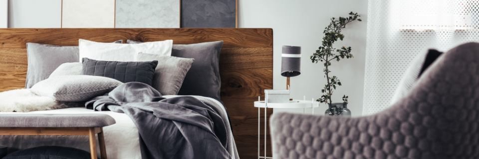 Accogliente camera da letto con letto, cuscini decorativi e una sedia imbottita in una palette di colori neutri.