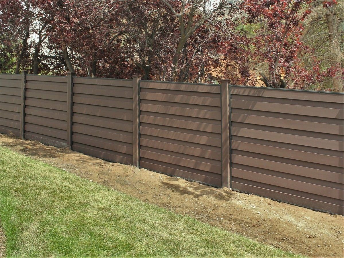 A wooden fence surrounds a lush green yard with trees in the background.
