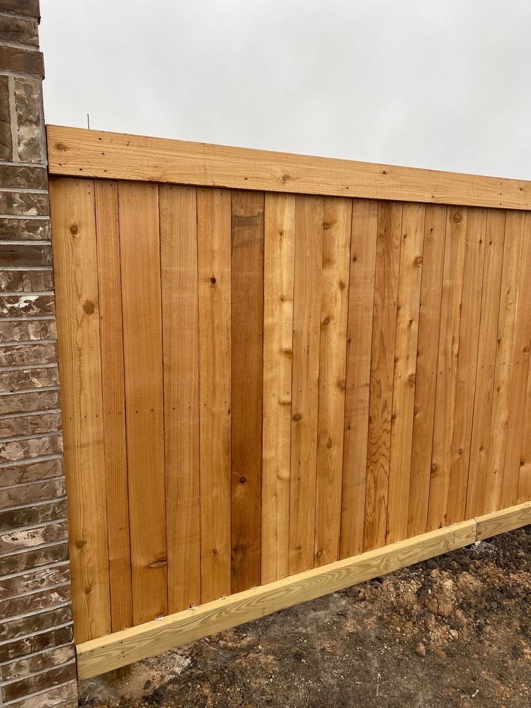 A wooden fence is sitting next to a brick wall.