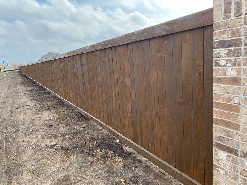 A wooden fence is sitting next to a brick wall.