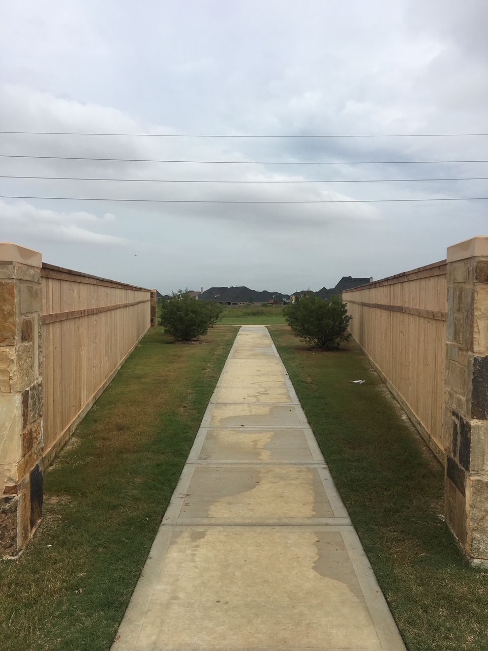 A concrete walkway between two wooden fences leading to a field.