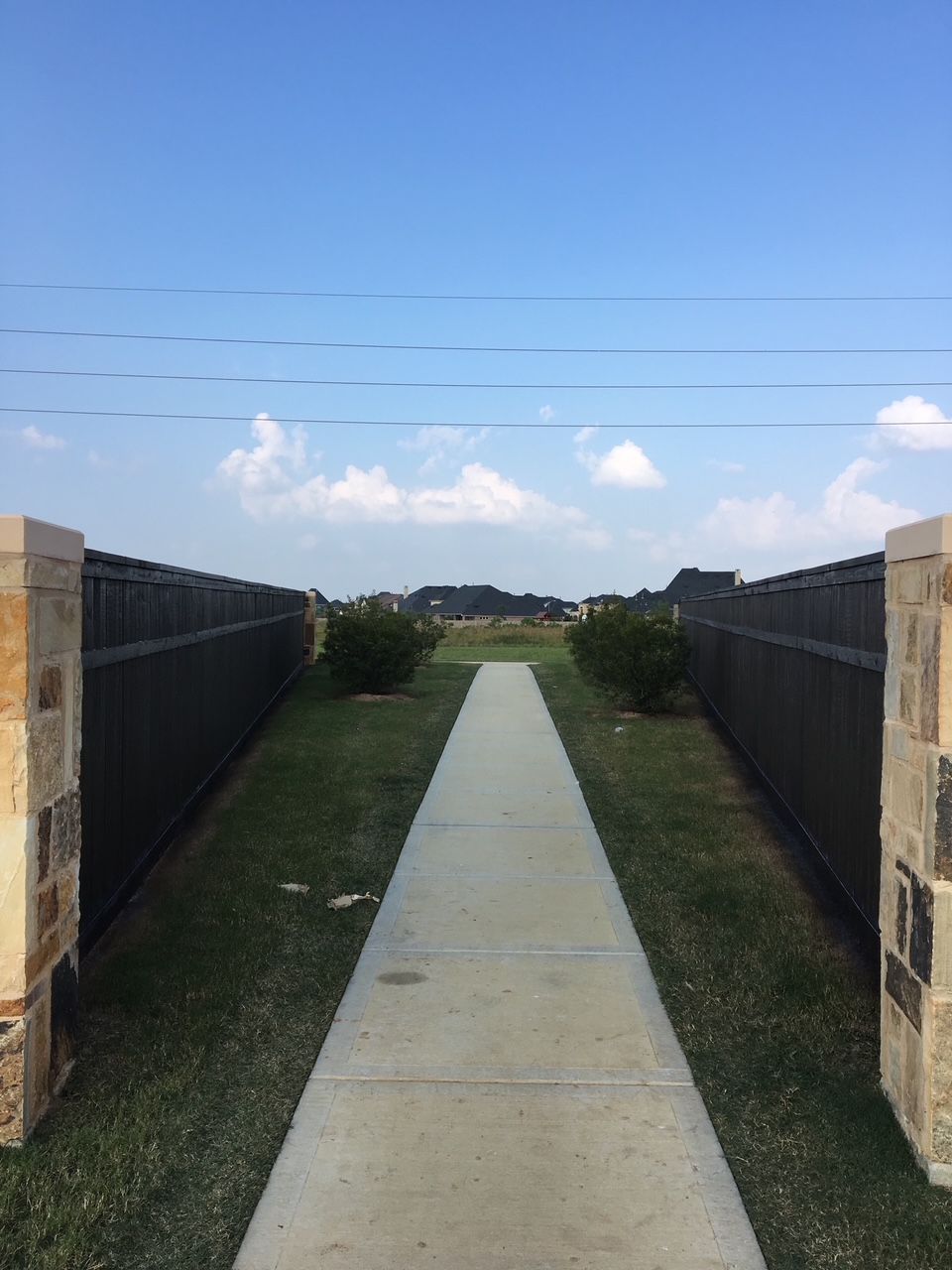 A concrete walkway between two fences leading to a field.