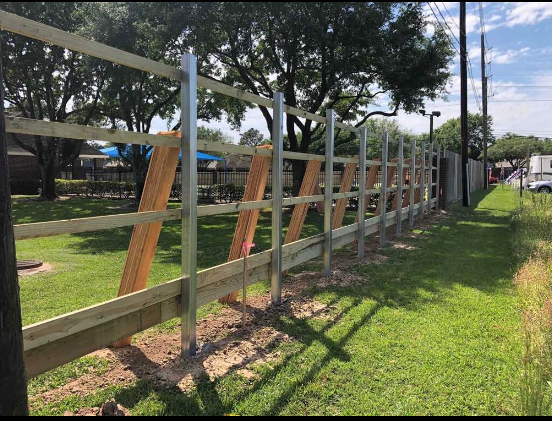 A wooden and metal fence is sitting in the middle of a grassy field.