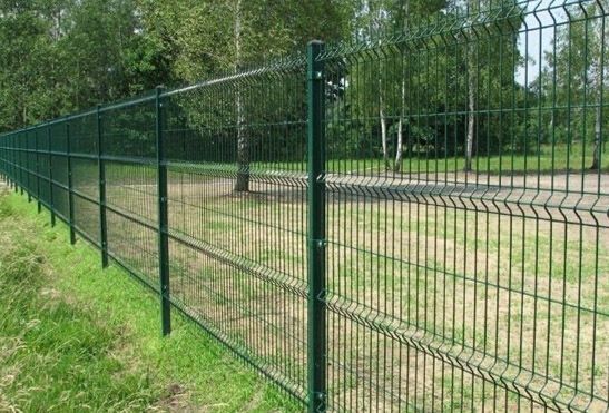 A green fence surrounds a grassy field in a park.