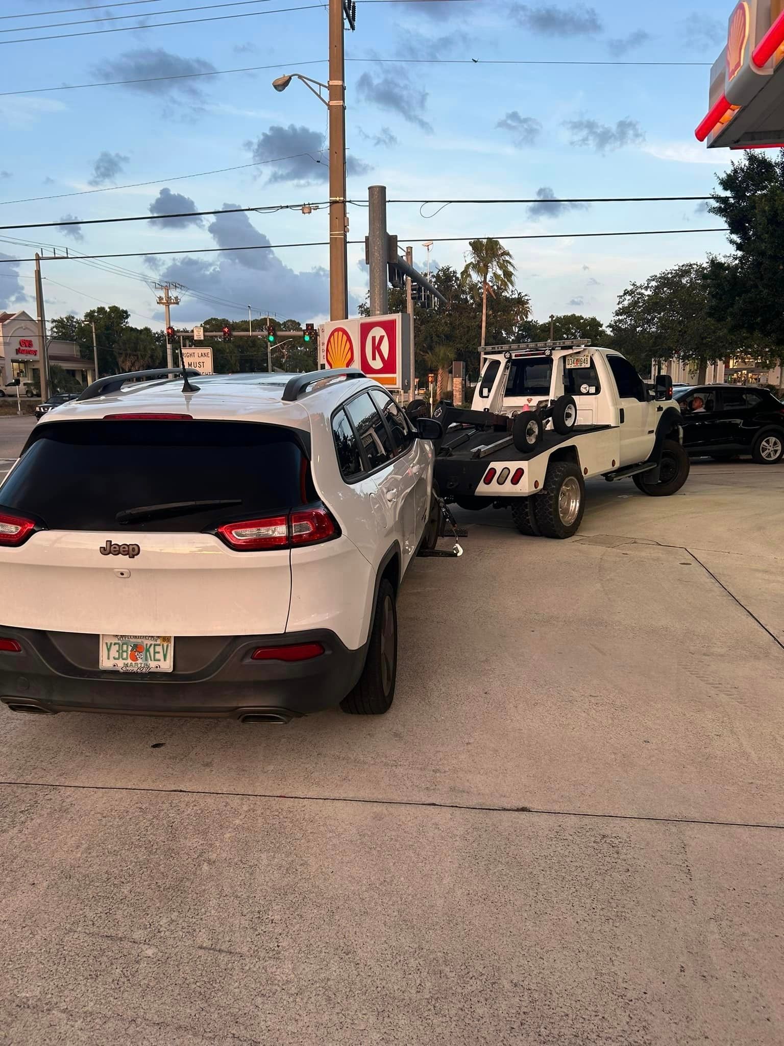A white jeep is parked in a parking lot next to a tow truck.