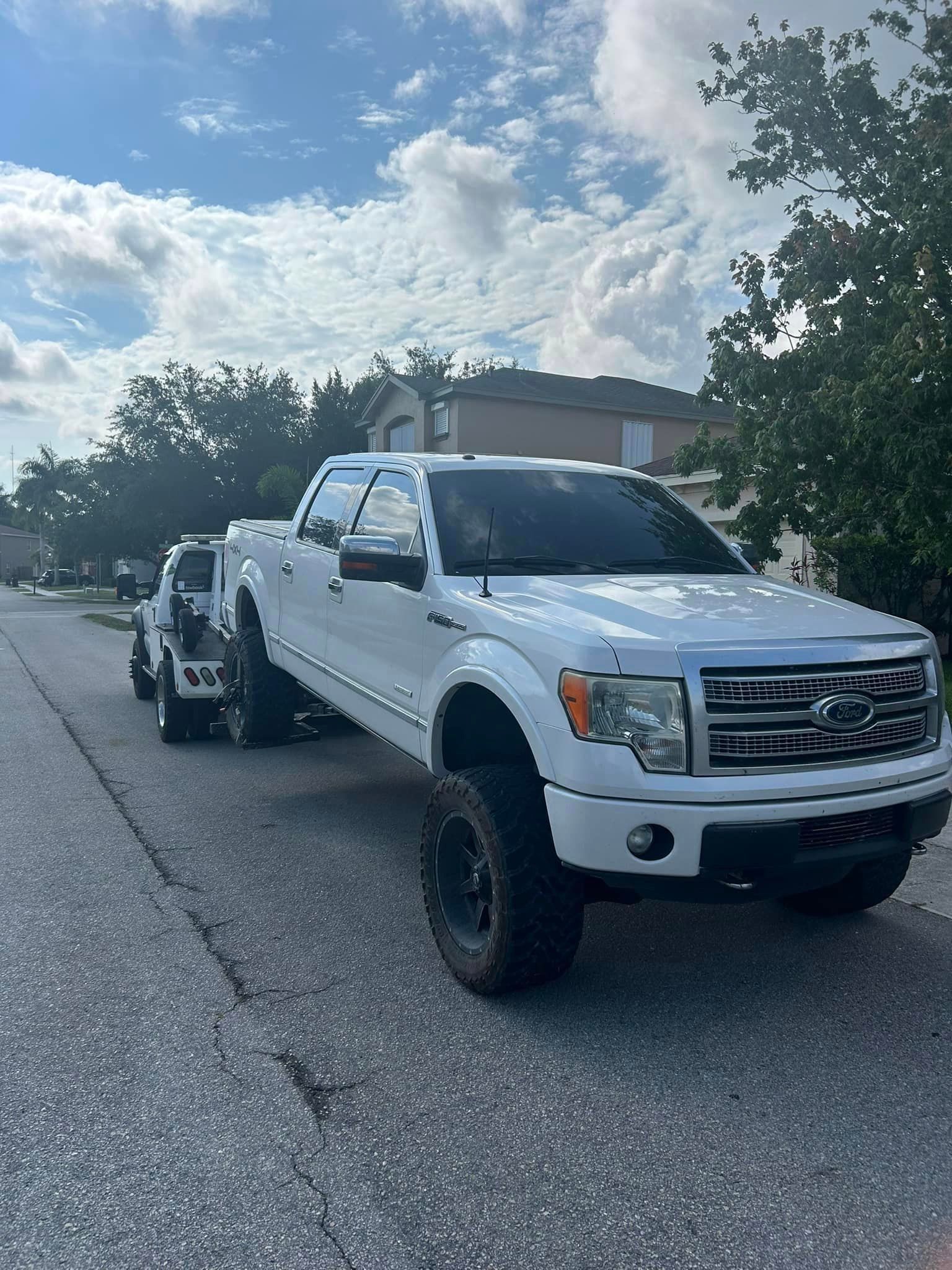 A white truck with a trailer attached to it is parked on the side of the road.