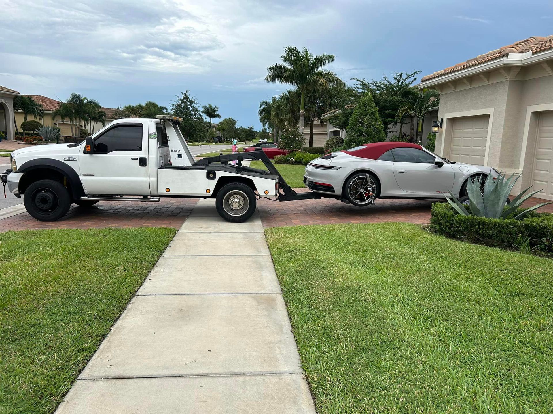 A white tow truck is towing a silver car in front of a house.