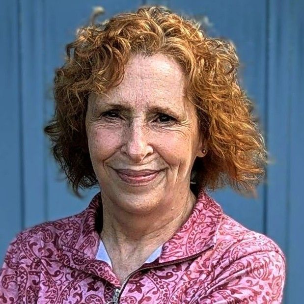 Portrait of a professional staff member wearing a pink patterned jacket, standing in front of a blue paneled background.