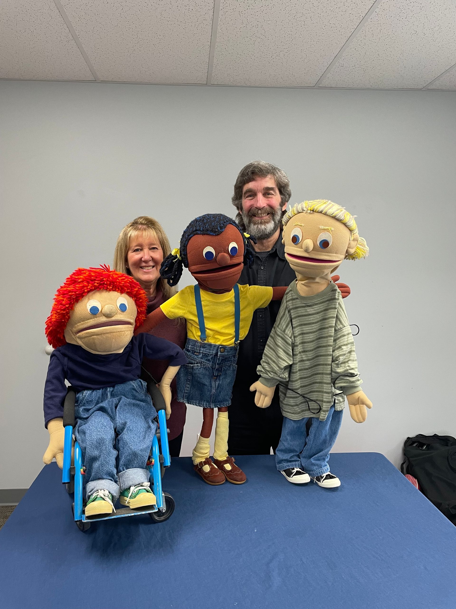 Smiling blonde haired woman and smiling brown haired man standing with three large puppets