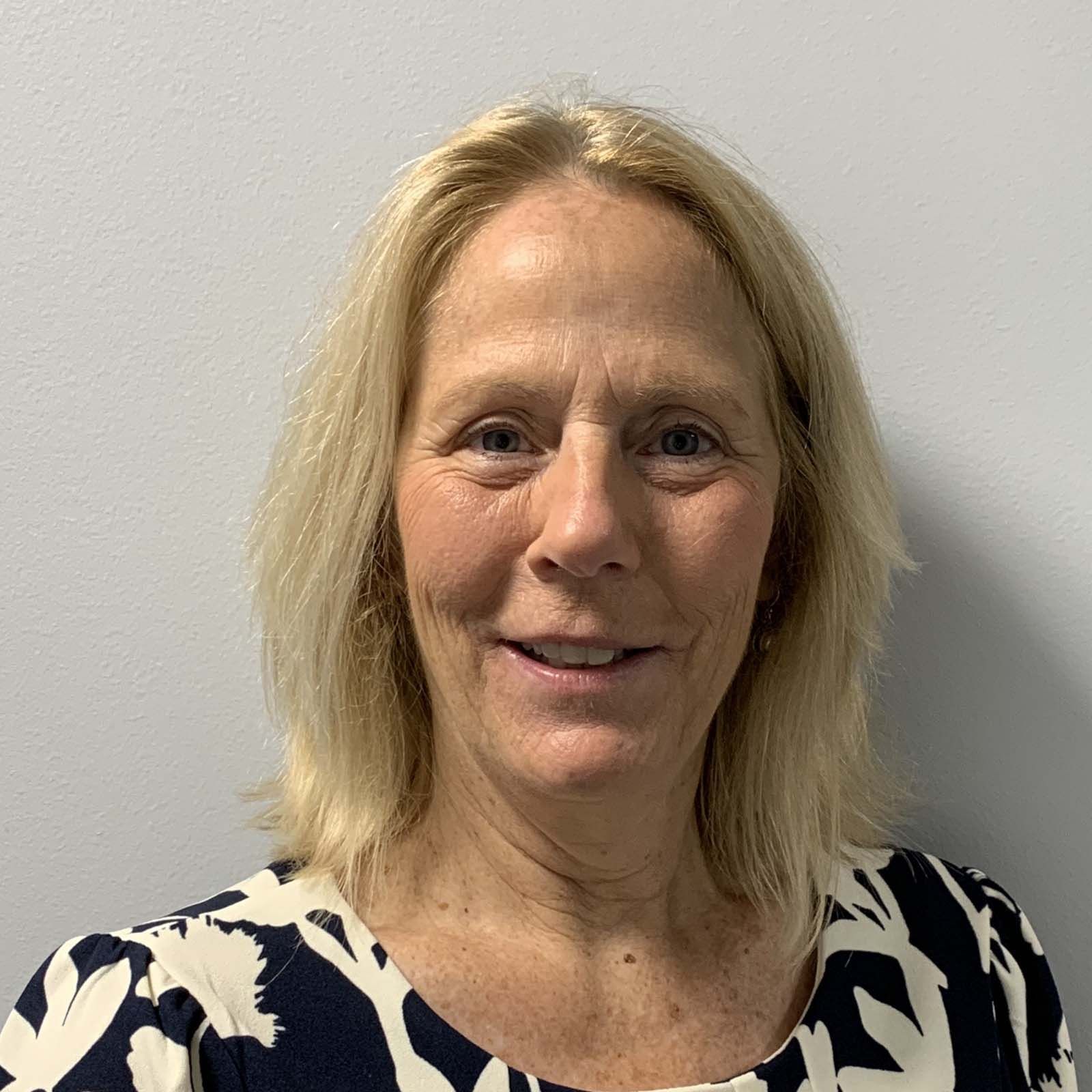 Portrait of a professional staff member wearing a patterned top, standing against a plain light-colored background.