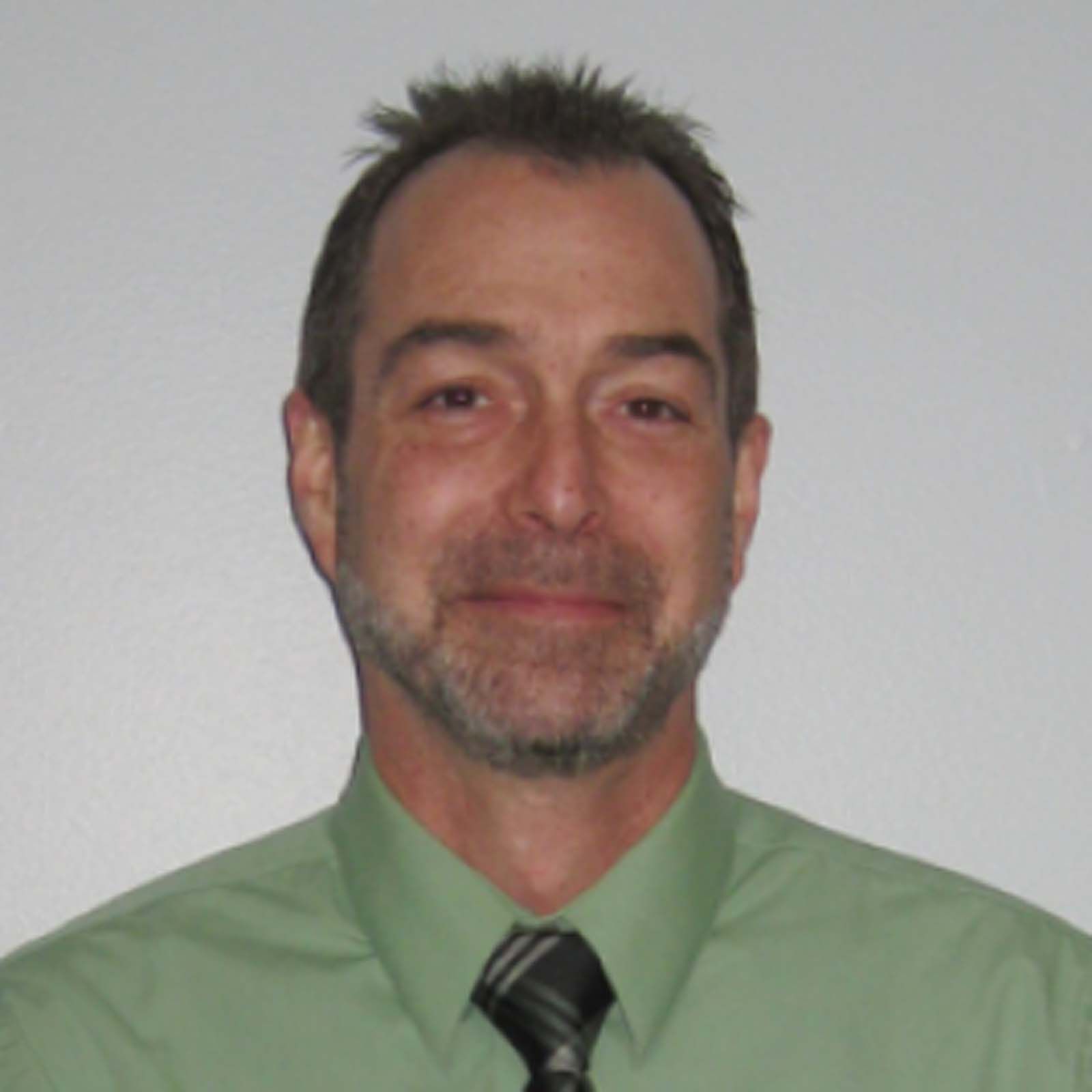 Portrait of a professional staff member wearing a green dress shirt and a dark patterned tie, standing against a plain light colored background.