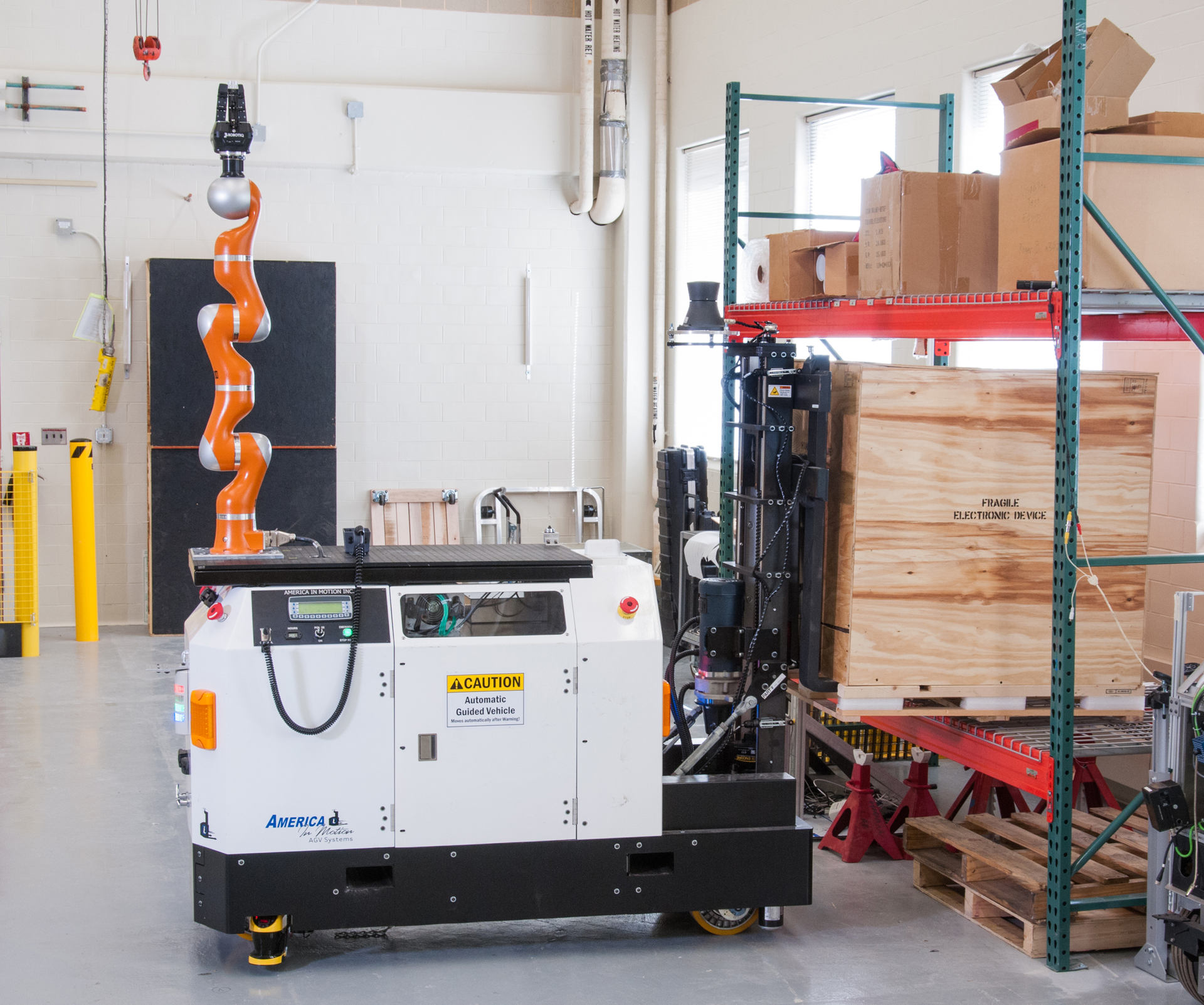 A robotic arm is attached to a white vehicle in a warehouse